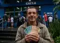 Homem segura notas de dinheiro em frente a uma agência da Caixa, em referência ao pagamento do seguro-desemprego em 2026.