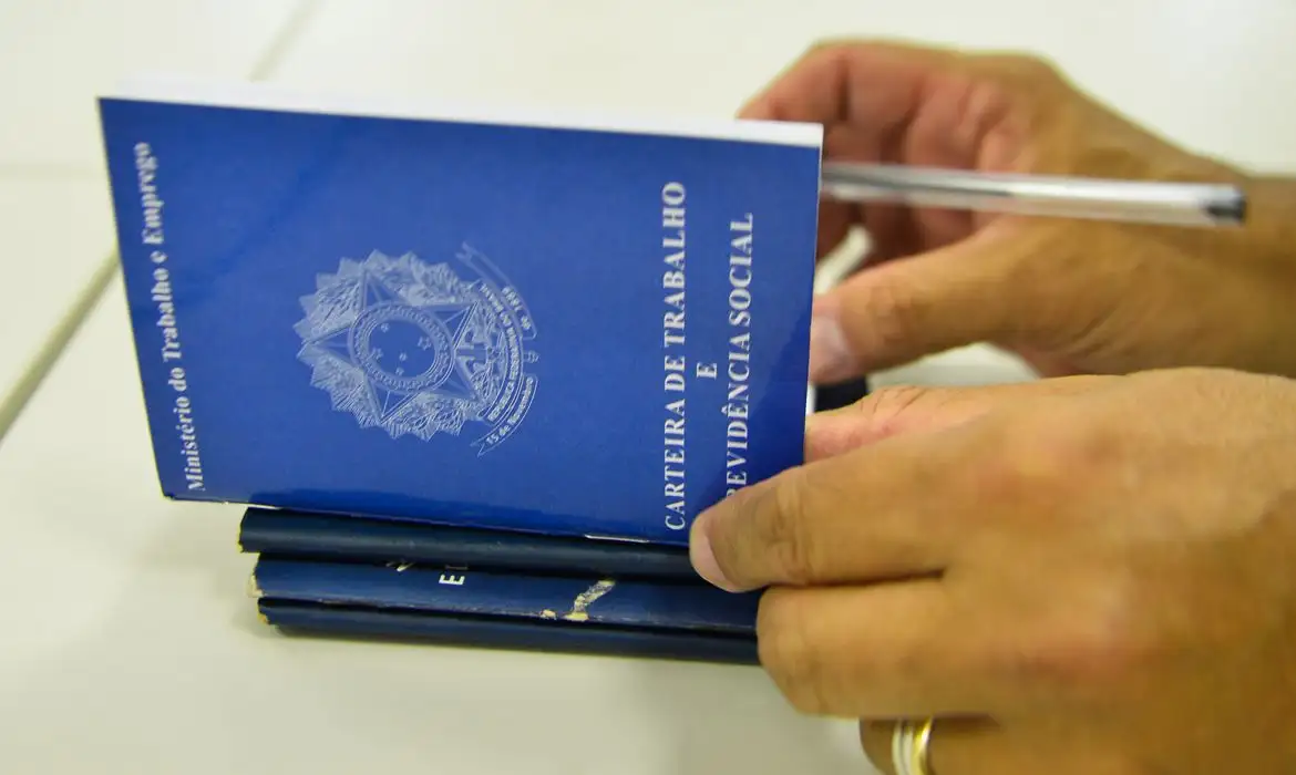 Mãos segurando carteiras de trabalho da Previdência Social, representando o pedido de seguro-desemprego do trabalhador demitido