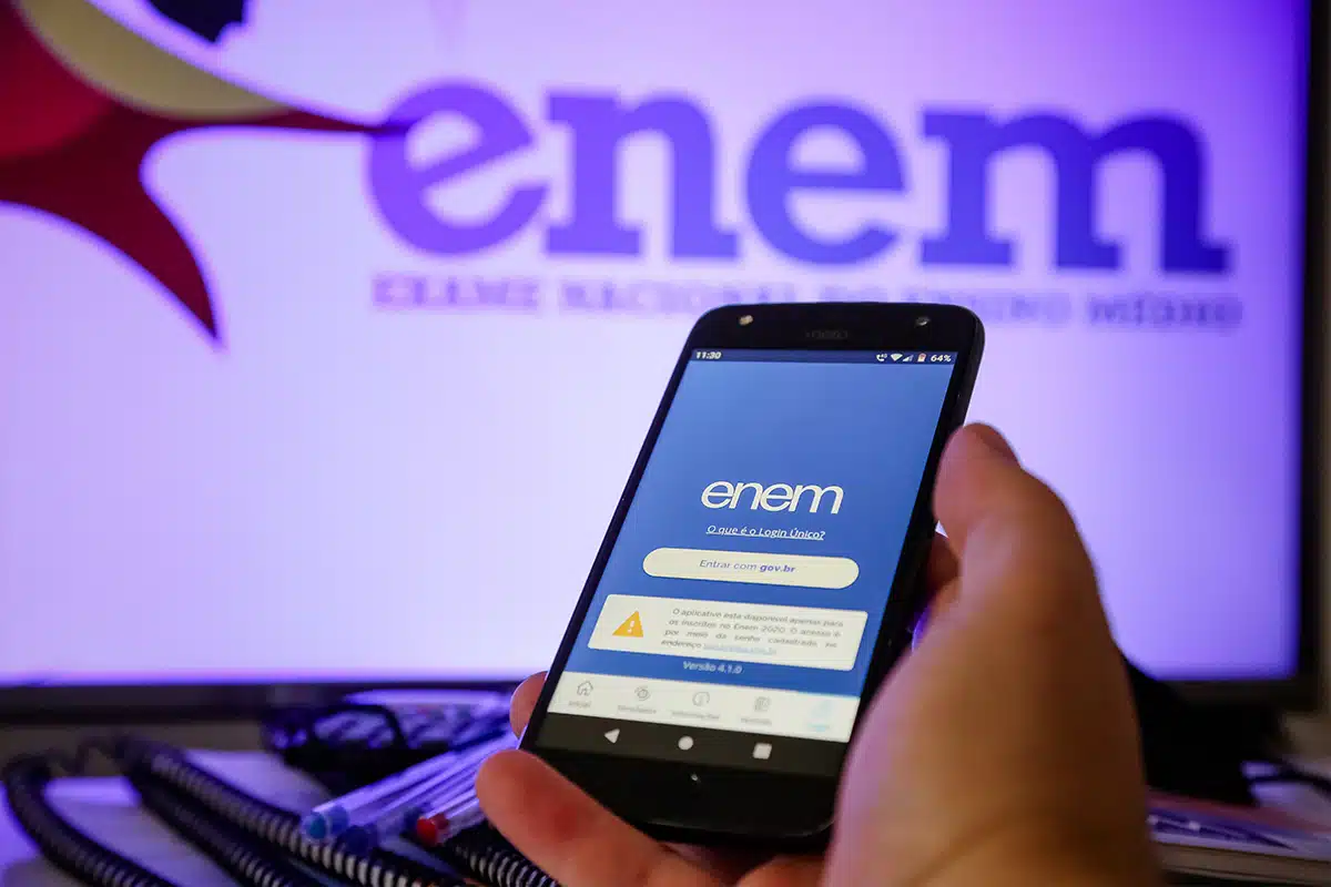 Pessoa acessando o aplicativo do Enem pelo celular, com destaque para orientações sobre gerar e pagar o boleto pela Página do Participante.