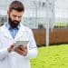 Profissional de jaleco analisa dados em tablet dentro de estufa de cultivo sustentável