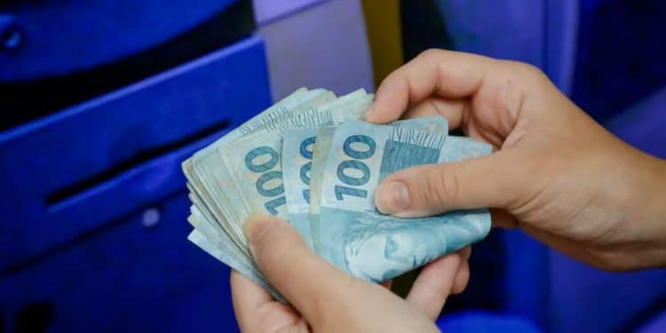 Pessoa conta cédulas de cem reais em frente a caixa eletrônico