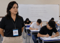 Fiscal de prova em sala de aula acompanhando candidatos durante exame.