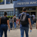 Pessoas caminhando em direção à Prefeitura Municipal com mochilas, bolsas e garrafas de água, representando candidatos de concurso público.