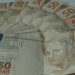 Notas de cinquenta reais espalhadas, representando os valores do abono salarial PIS/Pasep liberados em 2026.
