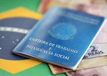 Carteira de trabalho sobre cédulas de real representa o pedido de antecipação do 13º salário durante as férias.