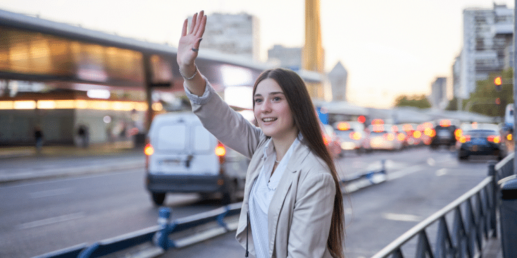 Jovem acena sorrindo no trânsito em avenida movimentada.