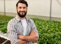 Jovem agricultor em estufa hidropônica com plantação de alfaces.