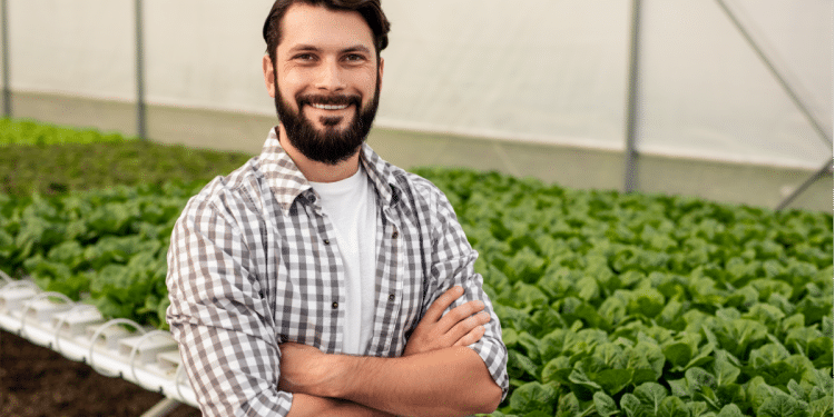 Jovem agricultor em estufa hidropônica com plantação de alfaces.