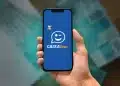 Aplicativo Caixa Tem exibido em smartphone com cédulas de reais.