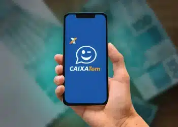 Aplicativo Caixa Tem exibido em smartphone com cédulas de reais.