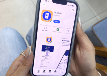 Pessoa segurando celular aberto na página do aplicativo e-Título.