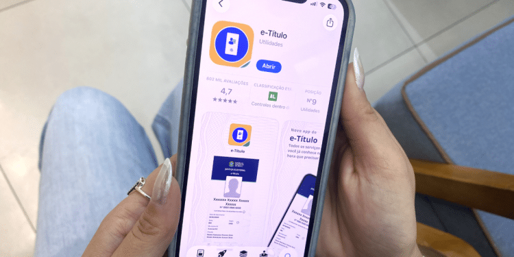 Pessoa segurando celular aberto na página do aplicativo e-Título.