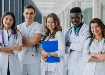 Equipe diversa de jovens profissionais da saúde sorrindo em corredor hospitalar.