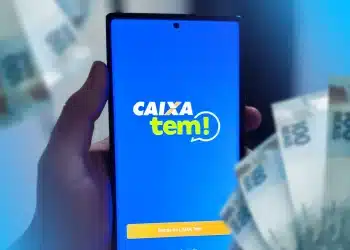 Mão segurando celular com tela do app Caixa Tem aberta e notas de cem reais ao fundo, simbolizando a movimentação do dinheiro do Pé-de-Meia pela conta Caixa Tem.