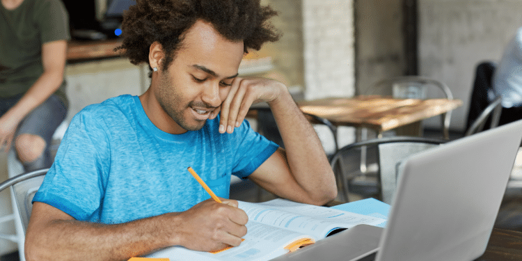 Jovem estudando com laptop em cafeteria moderna.