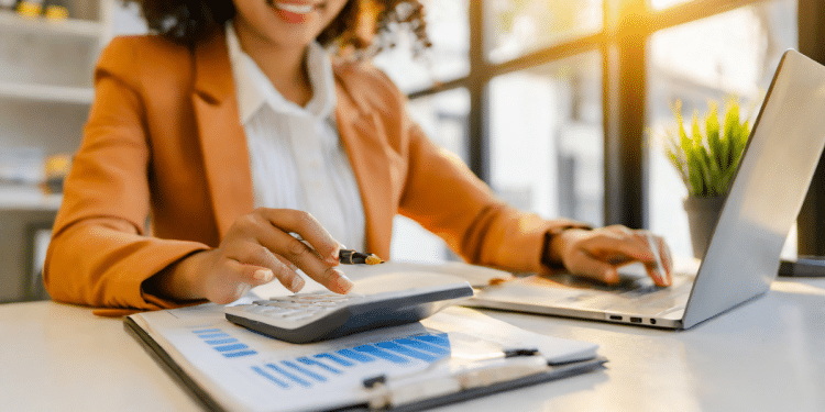 Jovem analisando finanças corporativas com calculadora e laptop em escritório iluminado.