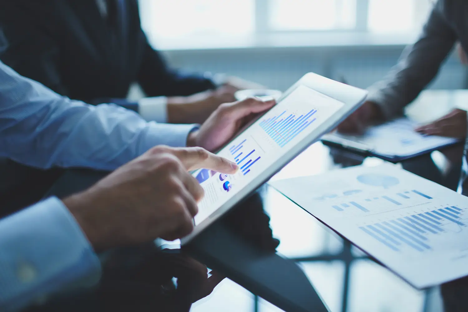 Profissionais analisam gráficos e indicadores financeiros em um tablet durante reunião de trabalho.