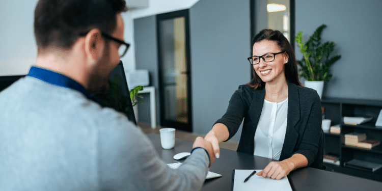 Entrevista de emprego com cumprimento entre recrutadora e candidato em escritório moderno.