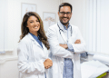 Médica e médico sorrindo em consultório iluminado.