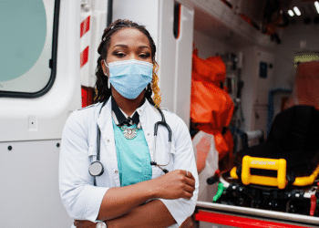 Mulher com máscara em frente a ambulância em plantão.