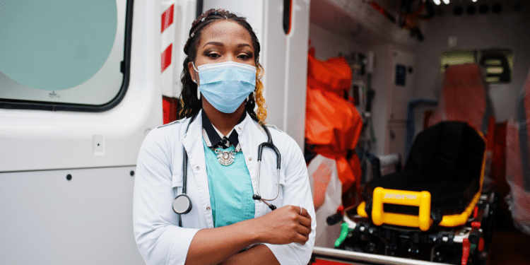Mulher com máscara em frente a ambulância em plantão.