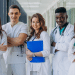 Jovens profissionais de saúde em uniforme posam em hospital.