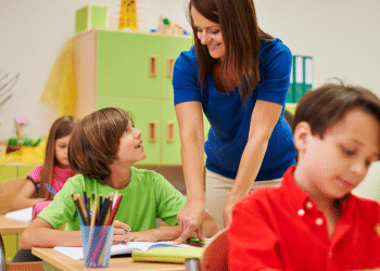 Professora orienta alunos em sala de aula colorida de ensino fundamental.