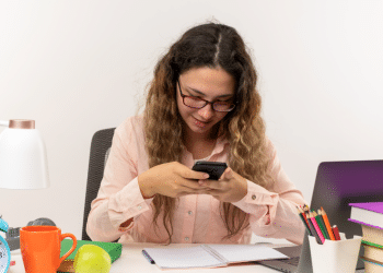 Jovem estudante distraída com celular em dia de estudos.