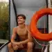 Salva-vidas sentado em embarcação de resgate com boia de segurança em ambiente aquático.