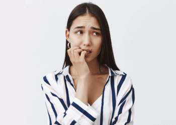 Mulher jovem ansiosa roendo unhas com expressão preocupada.
