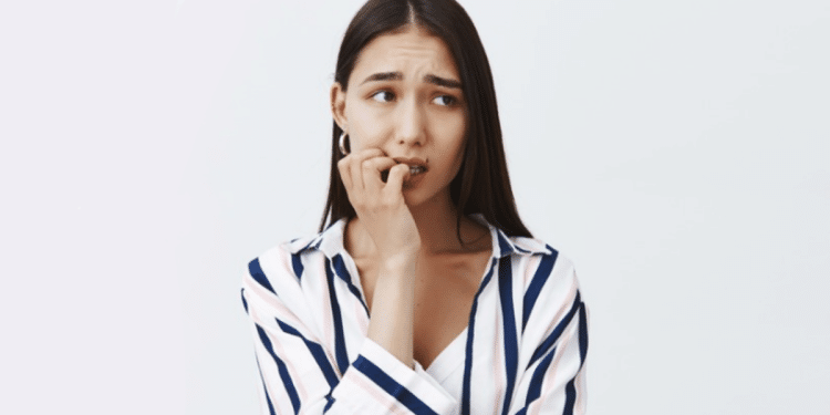 Mulher jovem ansiosa roendo unhas com expressão preocupada.