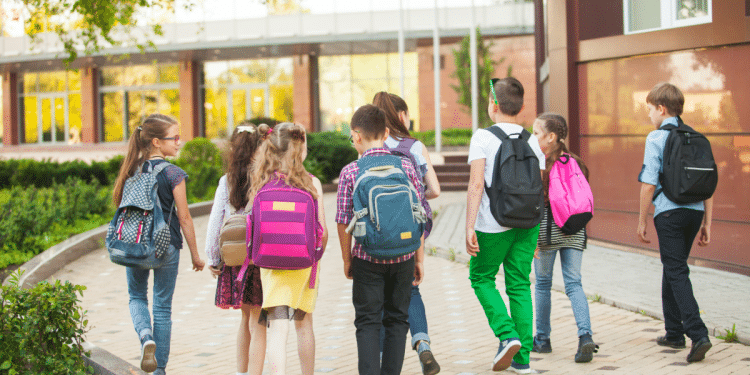 Grupo de crianças caminhando para escola em área externa.