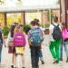 Grupo de crianças caminhando para escola em área externa.