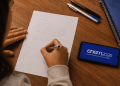 Jovem escreve redação sobre valorização da herança africana no Brasil ao lado de celular com tela do Enem 2026, simbolizando as formas de preparação para a redação do Enem 2026.