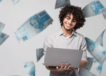 Jovem feliz trabalhando online com notas de 100 reais ao fundo.