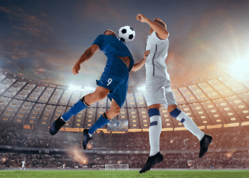 Jogadores duelam de cabeça em partida decisiva de futebol em estádio lotado.