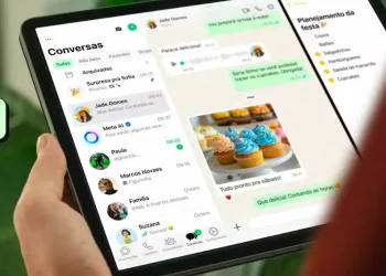 Pessoa segura um iPad com o WhatsApp aberto na tela de conversas e recursos de mensagens.