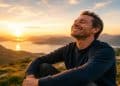 Homem sorri de olhos fechados diante do pôr do sol, transmitindo a paz de quem se libertou de sentimentos negativos