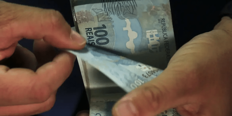 Mãos folheiam e conferem cédulas de cem reais uma a uma