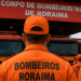 Bombeiros de Roraima em formação com fardas laranjas diante de viaturas do Corpo de Bombeiros Militar.