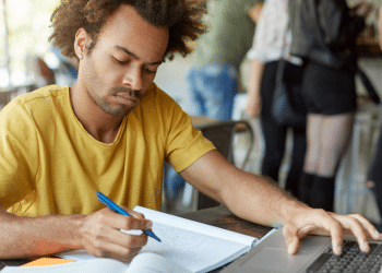 Candidato estuda com caderno e notebook para concursos públicos com vagas em São Paulo e Minas Gerais.