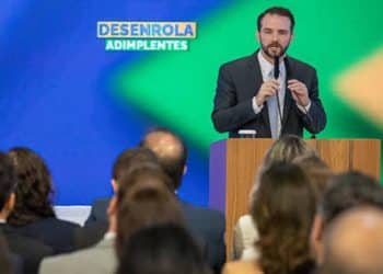 Homem de terno discursa em púlpito diante de plateia sob painel do Desenrola Adimplentes em evento do governo