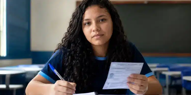 Estudante brasileiro em sala de aula segurando cartão de inscrição e caneta, em preparação para o Enem