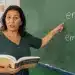 Professora de português explica na lousa a diferença entre “enfim” e “em fim” durante uma aula de gramática.