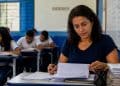 Professora corrige atividades em sala de aula da rede pública, ilustrando os salários dos docentes da rede estadual e o estado que mais paga.