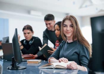 Grupo de jovens em ambiente de trabalho, com computadores e livros sobre a mesa