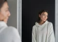 Mulher observando o próprio reflexo no espelho, representando a reflexão pessoal e o hábito de falar sozinho.