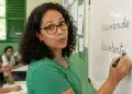 Professora escrevendo “descoberto” no quadro em sala de aula, representando a forma correta entre “descoberto” e “descobrido”.