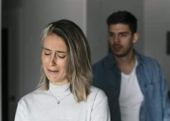 Mulher de cabelos loiros curtos chorando, homem ao fundo com expressão séria, simbolizando as frases para nunca dizer a quem se ama.
