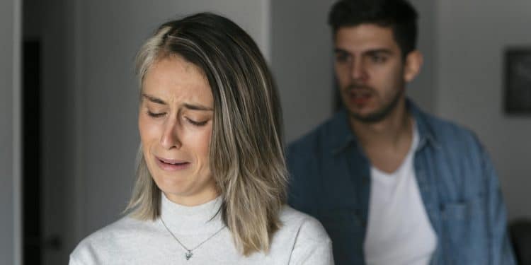 Mulher de cabelos loiros curtos chorando, homem ao fundo com expressão séria, simbolizando as frases para nunca dizer a quem se ama.